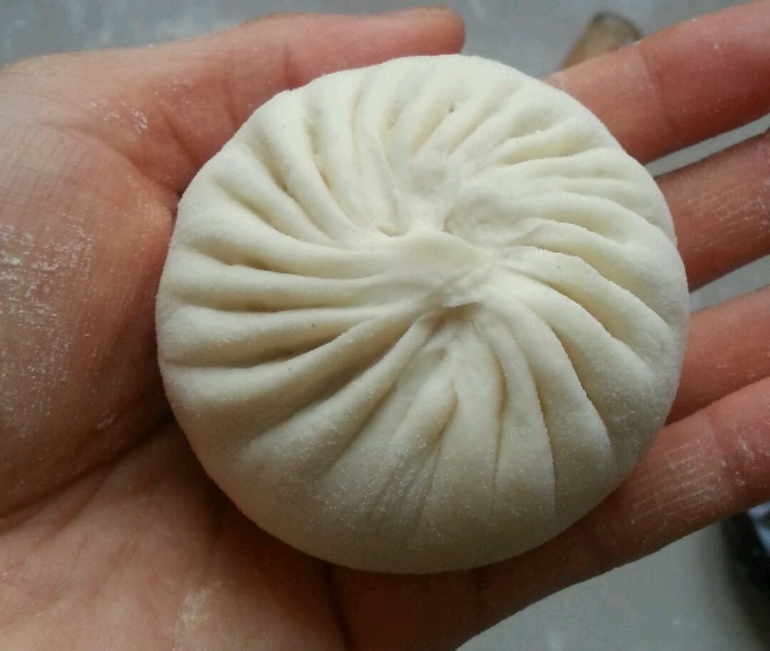 将放入馅的包子放入左手掌中,右手捏住包子皮的边,从一个褶开始一个