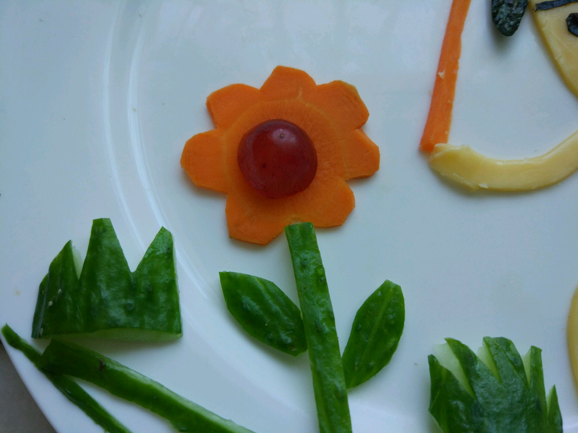 胡萝卜做成花朵,花蕊用了半个葡萄,黄瓜做成花茎和叶子还有小草.