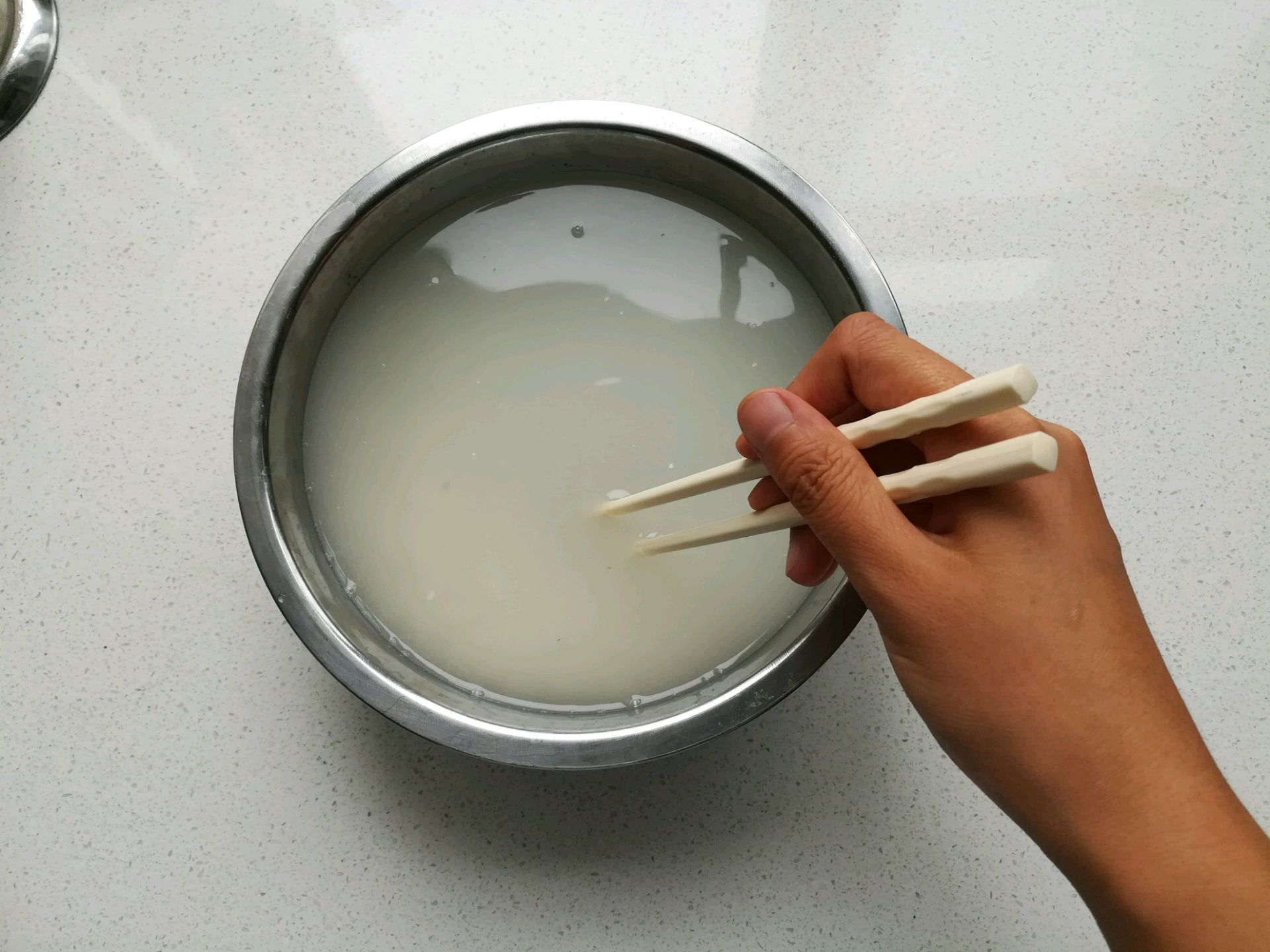在大米中倒入清水,用筷子划圈搅拌大米,多换几次水,把大米淘洗干净.