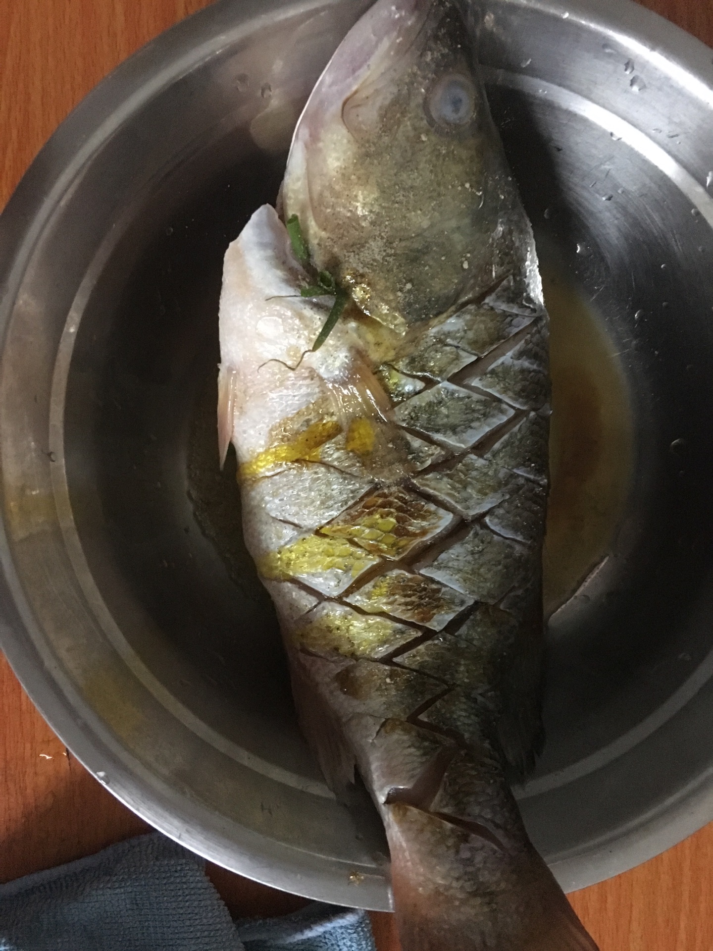 鲈鱼改刀切花,抹上盐,糖,胡椒粉,鱼肚塞入香葱,生姜,淋上少许油,撒上