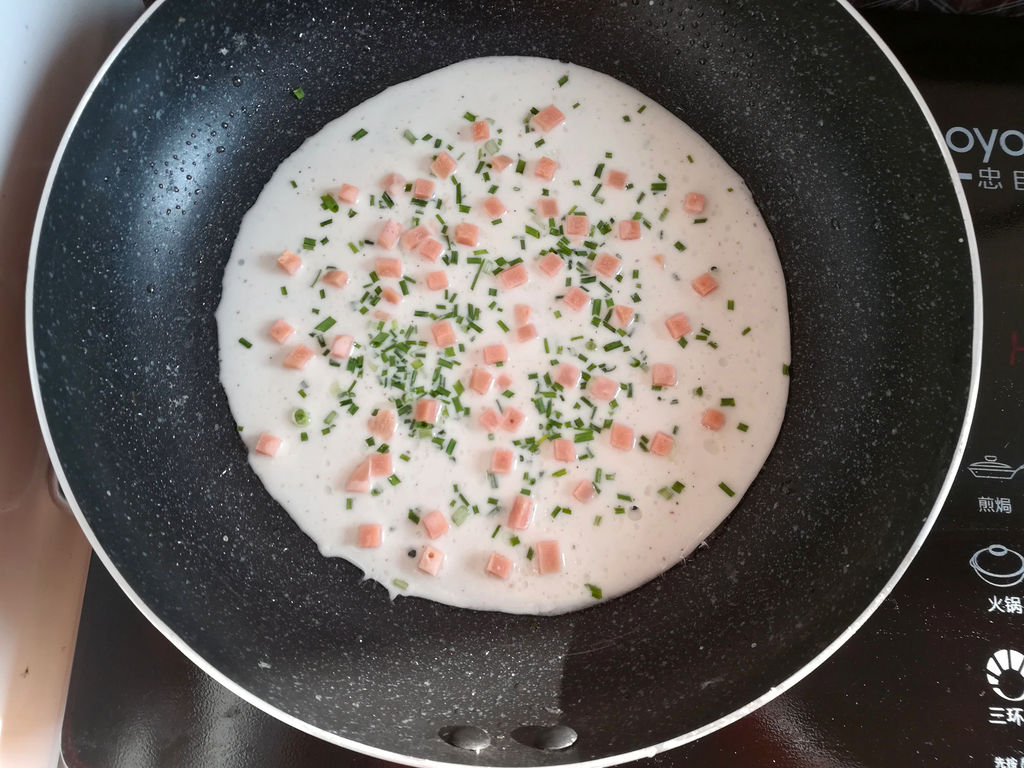 在面糊上撒上适量的野葱碎和火腿肠丁,开小火煎饼